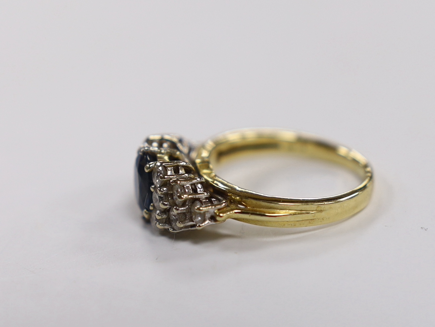 A modern 18ct gold and single stone oval cut sapphire set dress ring, with twelve stone diamond set shoulders, size O, gross weight 6.7 grams.